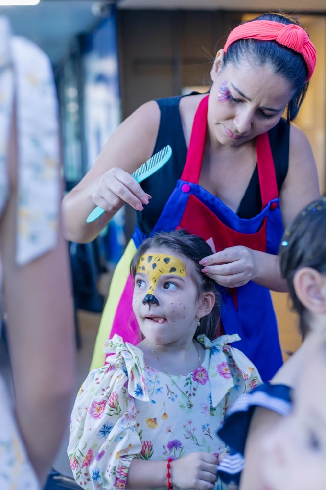 Recreadora penteando uma menina que está com o rosto pintado de onça