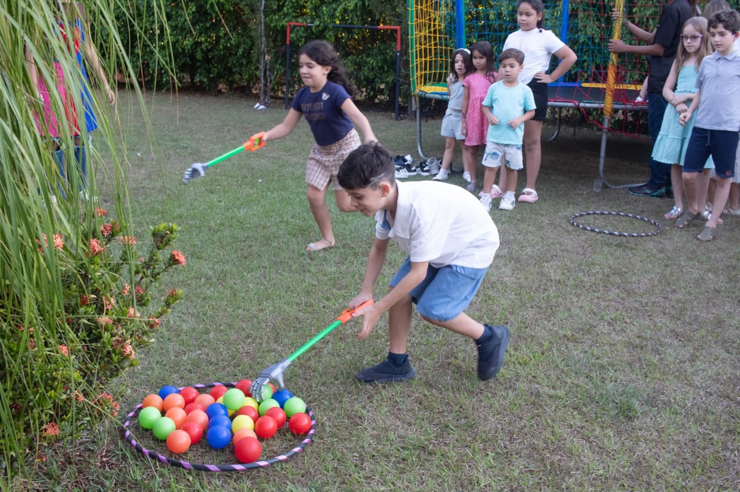 Duas crianças correndo para pegar bolinhas coloridas com garras de brinquedo