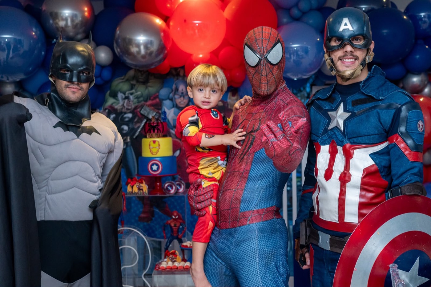 Menino no colo do Homem-Aranha com o Batman e o Capitão América ao lado