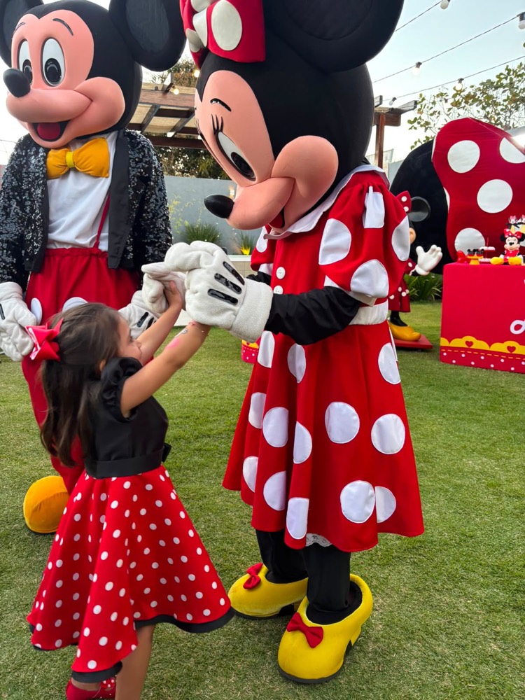 Menina de vestido de bolinhas dançando de mãos dadas com a Minnie e o Mickey